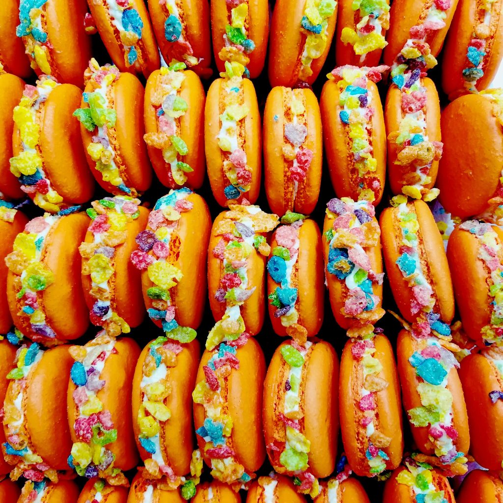 Rows of orange macarons rolled in colorful fruity cereal