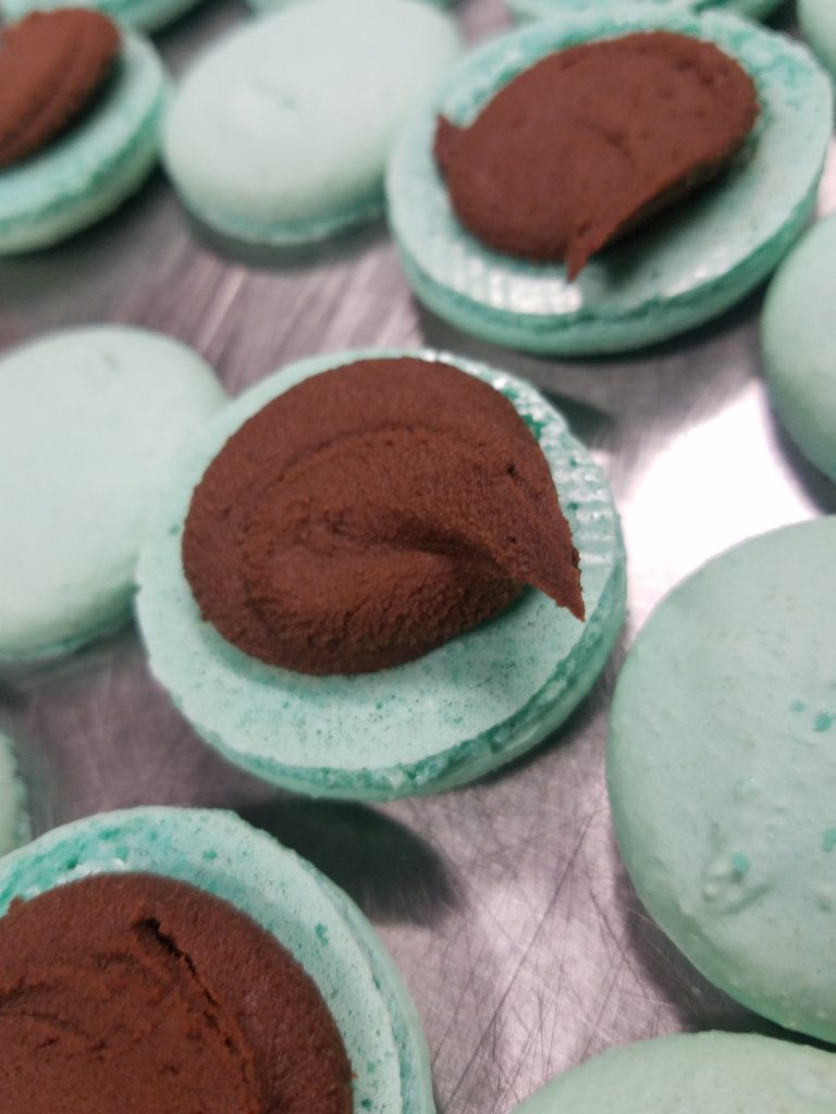 Mint green macaron shells being filled with chocolate ganache